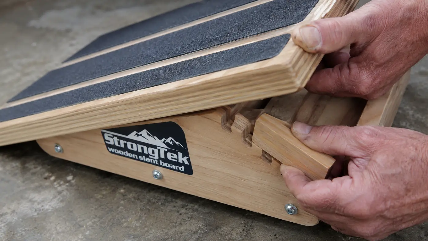 Close-up of hand adjusting the wooden peg on a slant board to lock in a steeper angle