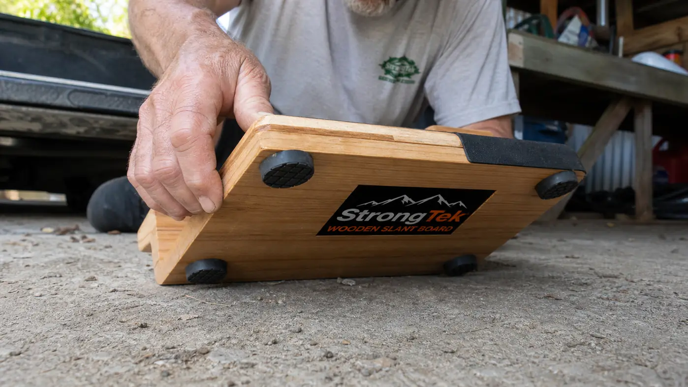 Wooden slant board sitting flush against a concrete garage floor with visible non-slip pad texture underneath